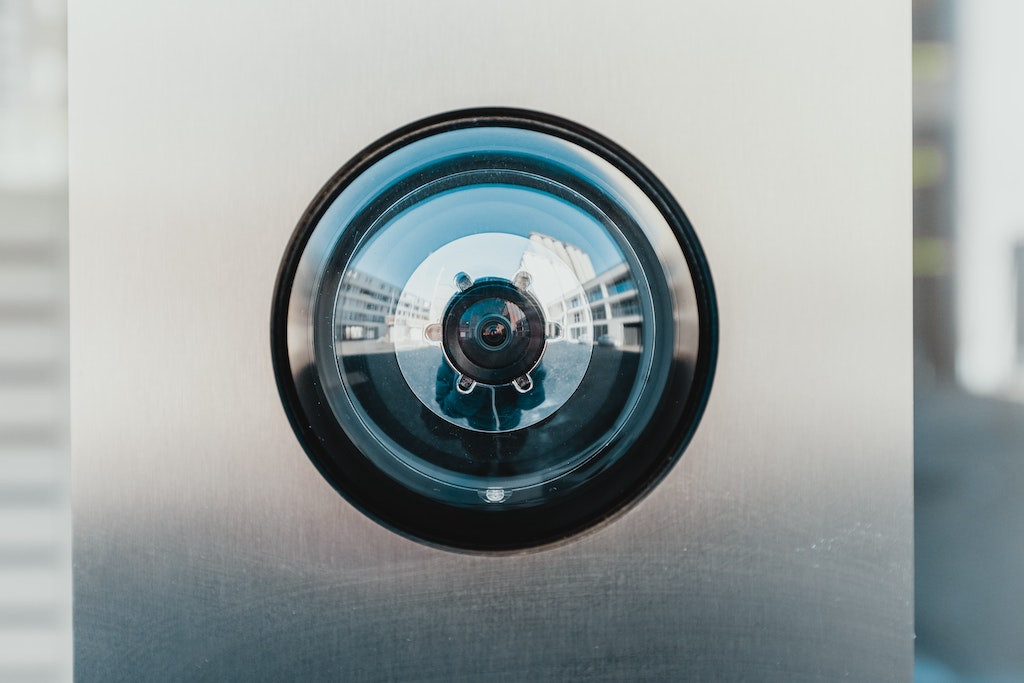 A closeup of an outdoor security surveillance camera, showing parts of the photographer in the reflection