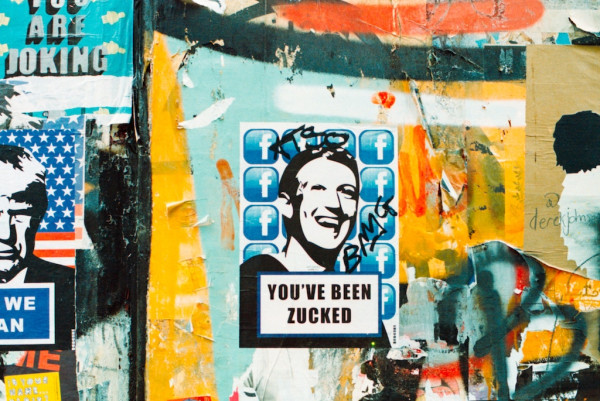 On a graffitied wall, a stencil of Facebook founder and CEO Mark Zuckerberg's facebook, surrounded by FB logos and overlayed with the phrase YOU'VE BEEN ZUCKED