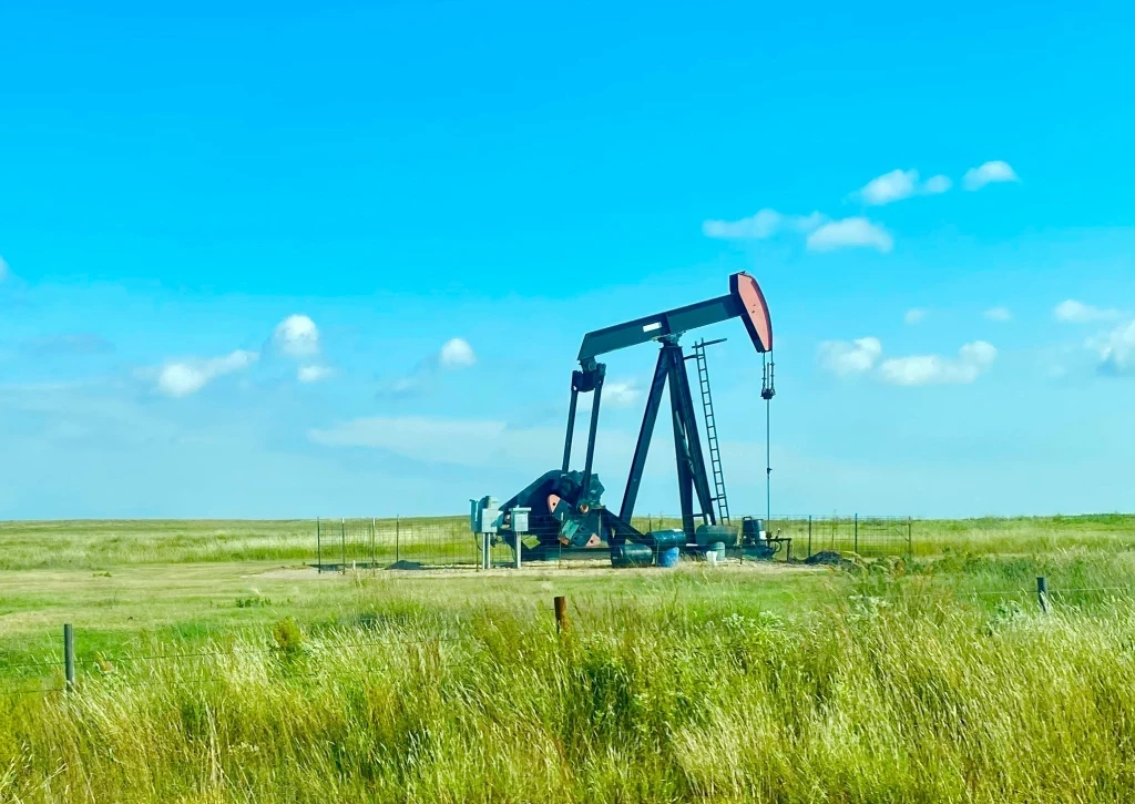 An oil pump in the middle of a field on a bright sunny day.