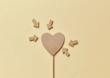 Creative composition of a cardboard heart with arrows on a yellow background, perfect for conceptual design.