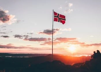 A Norweigan flag on a mountain top while the sun sets behind it