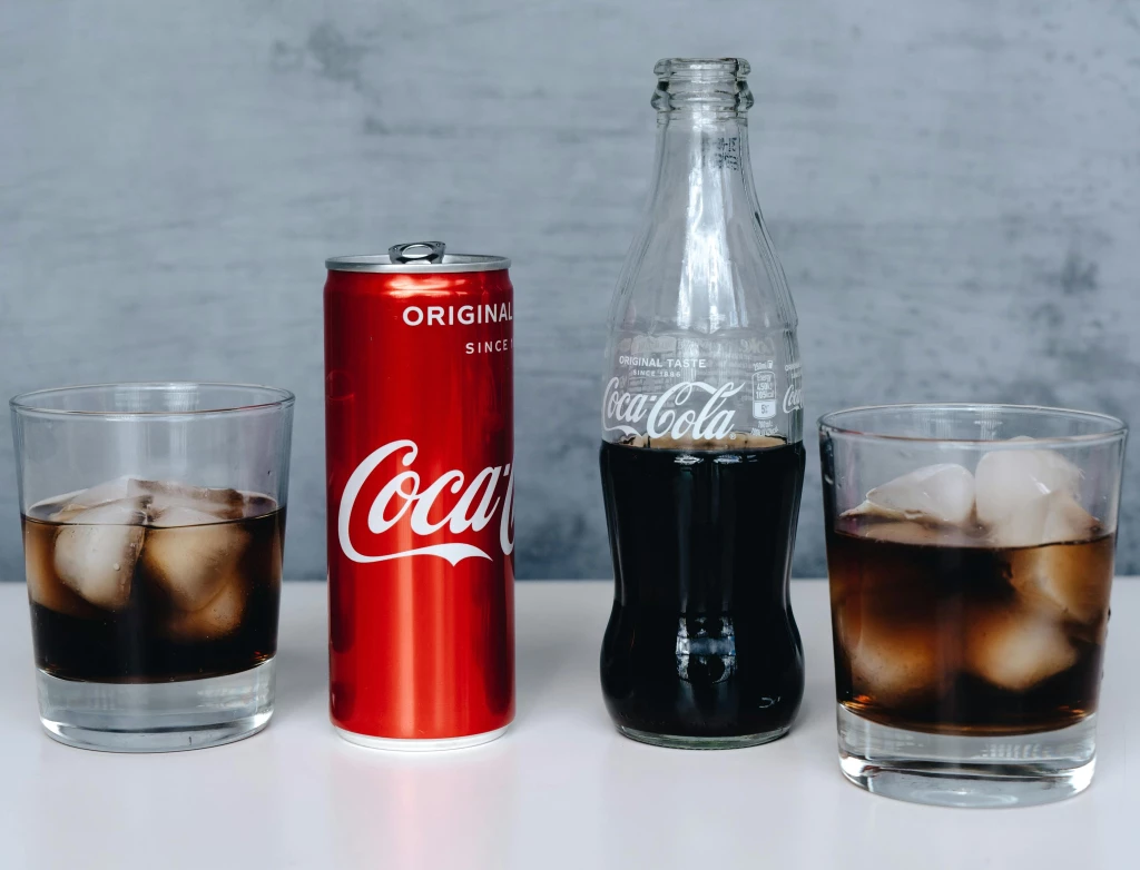 coca cola can and bottle with drinks poured in tumblers over ice