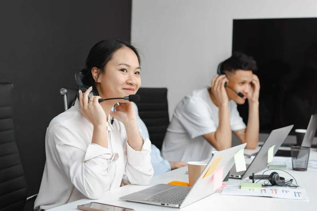 customer service agent holding headphones at desk with laptop