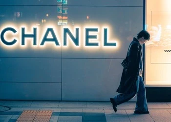 Stylish woman walking past a lit Chanel storefront at night, showcasing urban fashion and city life