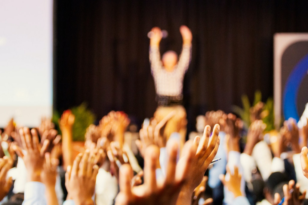 employee engagement, demonstrated by an auditorium of hands raised in the air in response to a presentation by a senior leader, who is also holding their hands up